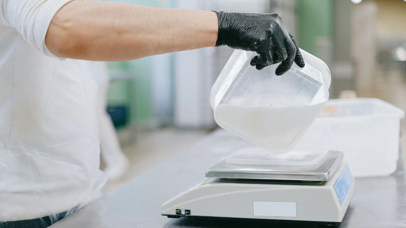 Una mano con guante vierte un ingrediente en una báscula de cocina